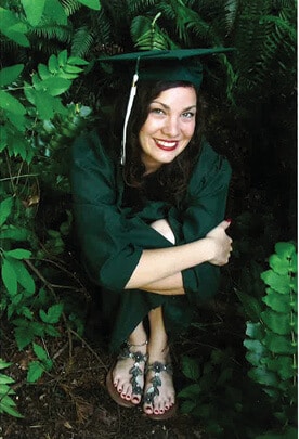 Portrait of Erica Cronin sitting down wearing her green cap and gown and smiling at the camera